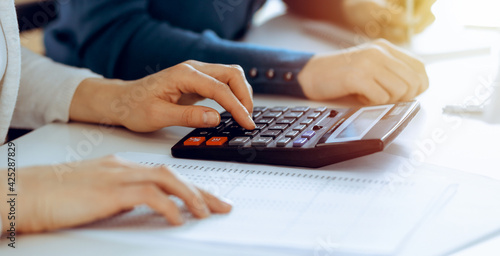 Accountant checking financial statement or counting by calculator income for tax form, hands closeup. Business woman sitting and working with colleague at the desk in office. Tax and Audit concept