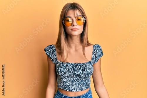 Teenager caucasian girl wearing fashion yellow sunglasses with serious expression on face. simple and natural looking at the camera.