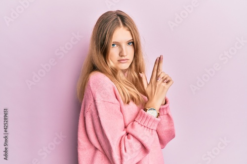 Beautiful young caucasian girl wearing casual clothes holding symbolic gun with hand gesture, playing killing shooting weapons, angry face