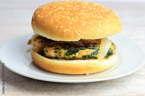 Homemade meat burger with vegetables, spinach. Served on a small white plate, wooden base.