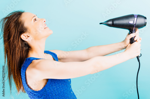 Beautiful young woman drying her hair with blow dryer smiling with blue background. hair care concept hairdresser