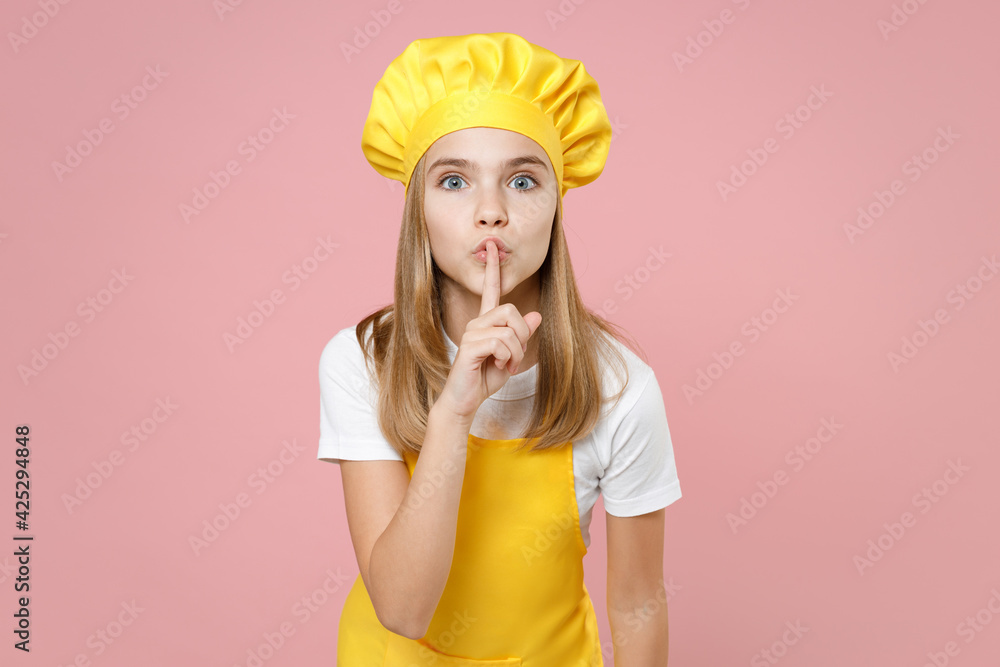 Teen secret girl chef cook confectioner baker housewife wear yellow apron white t-shirt cap saying hush be quiet with finger on lips shhh gesture isolated on pink background studio Food cake concept. Teen secret girl chef cook confectioner baker housewife wear yellow apron white t-shirt cap saying hush be quiet with finger on lips shhh gesture isolated on pink background studio Food cake concept.