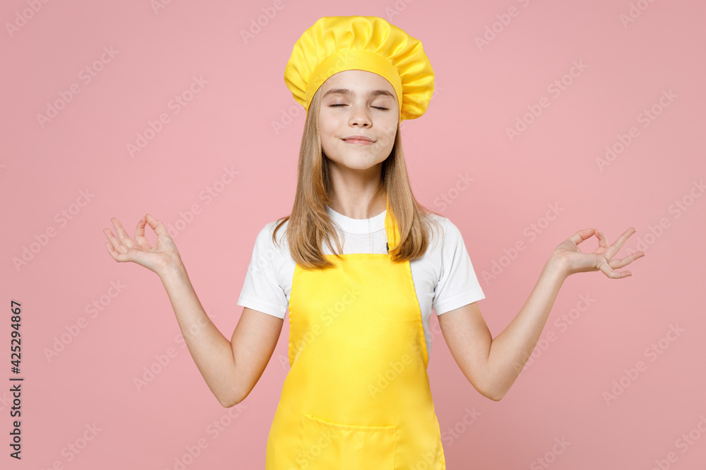 Teen girl chef cook confectioner baker housewife in yellow apron white t-shirt cap hold spread hands in yoga gesture relax meditate try calm down isolated on pink background studio Food cake concept. Teen girl chef cook confectioner baker housewife in yellow apron white t-shirt cap hold spread hands in yoga gesture relax meditate try calm down isolated on pink background studio Food cake concept.