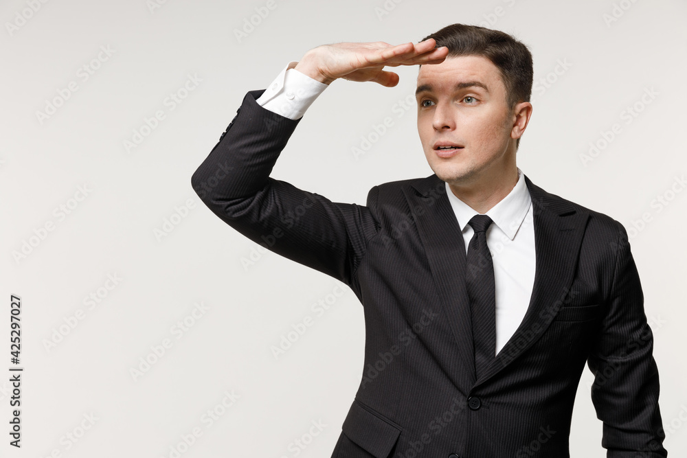 Young waiting employee business corporate lawyer man 20s wear classic formal black grey suit shirt tie work in office hold hand at forehead look far away distance isolated on white background studio. Young waiting employee business corporate lawyer man 20s wear classic formal black grey suit shirt tie work in office hold hand at forehead look far away distance isolated on white background studio.