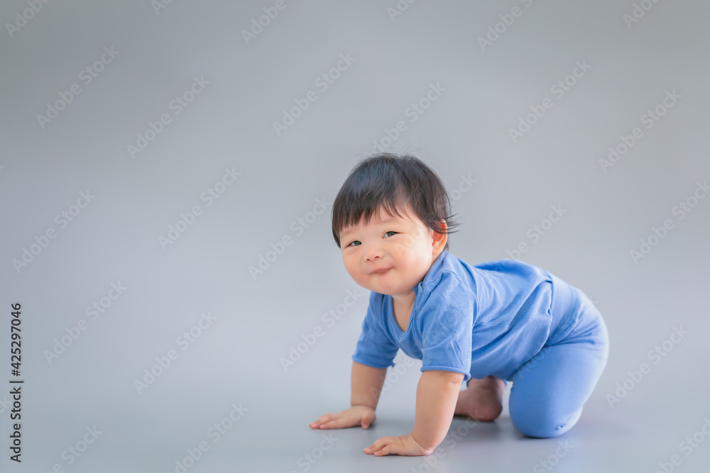 Asian happy cute baby smiling, sitting on gray background. 6 months baby in blue cloth on copy space as concept of bedroom, development, health, mood and motion of baby and kid department in hospital