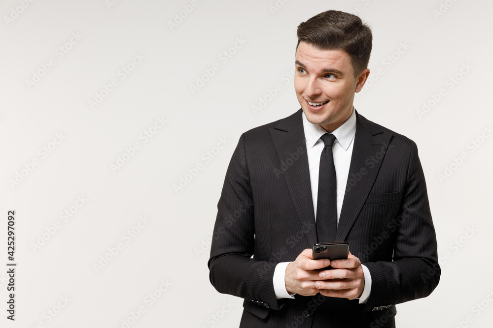 Young successful employee business corporate lawyer man wear classic formal black grey suit shirt tie work in office hold mobile cell phone look aside isolated on white background studio portrait. Young successful employee business corporate lawyer man wear classic formal black grey suit shirt tie work in office hold mobile cell phone look aside isolated on white background studio portrait.
