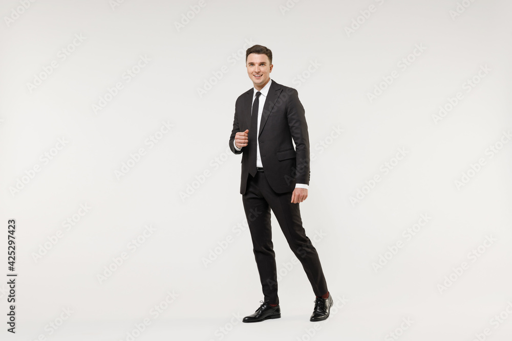 Full length young happy smiling successful employee business corporate lawyer man wear classic formal black grey suit shirt tie work in office walk going isolated on white background studio portrait. Full length young happy smiling successful employee business corporate lawyer man wear classic formal black grey suit shirt tie work in office walk going isolated on white background studio portrait.