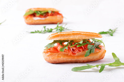 Eclair with salted trout, cream cheese and arugula on the white table