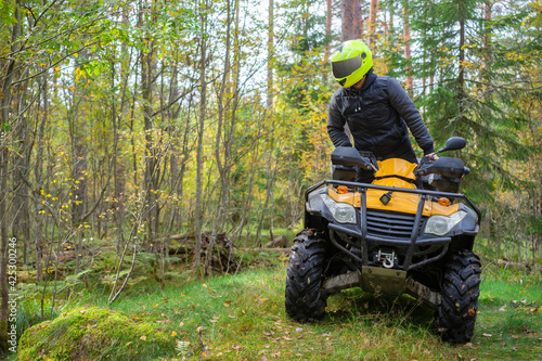 Biker rides a woodland. ATV driver got up to look around. Biker on a yellow ATV. Quad bike driver drive off road. He is into extreme driving. Concept - off-road ATV race. Hobby extreme sport.