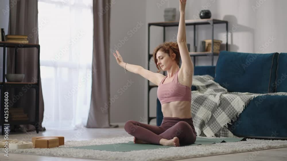 adult woman is training at home at weekend, sitting in lotus position on floor in room and doing exercises adult woman is training at home at weekend, sitting in lotus position on floor in room and doing exercises