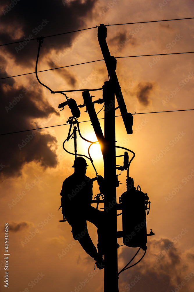 The silhouette of power lineman climbing on an electric pole with a  transformer installed. And replacing the damaged hotline clamp, bail clamp,  dropout and surge arrester that causes a power failure. Photos