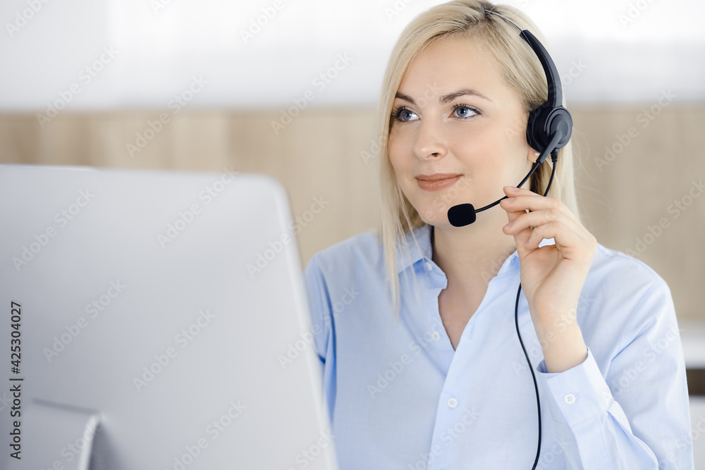 Blonde business woman sitting and communicated by headset in call center office. Concept of telesales business or home office occupation Blonde business woman sitting and communicated by headset in call center office. Concept of telesales business or home office occupation