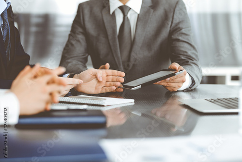 Unknown businessman using tablet computer and working together with his colleague while sits at the glass desk in modern office. Teamwork and partnership concept