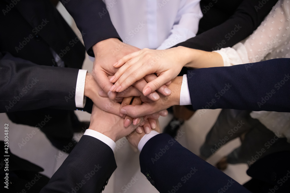 Crop close up top view of multiracial employees colleagues stack hands in pile show team loyalty and unity. Diverse multiethnic businesspeople engaged in teambuilding activity. Teamwork concept.