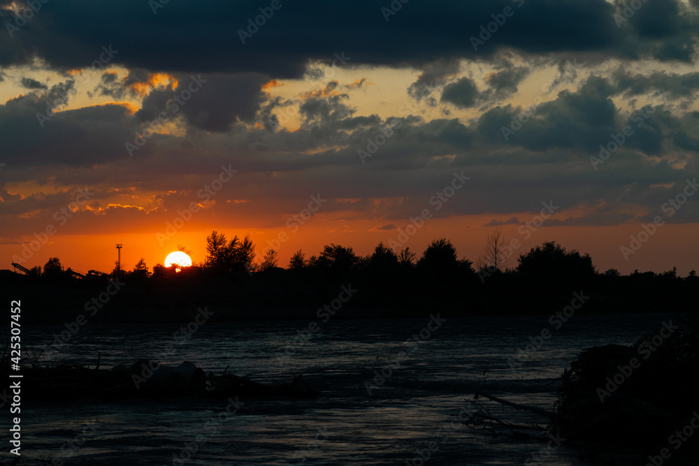 Evening sunset on the background of trees and antennas, in the foreground the river.