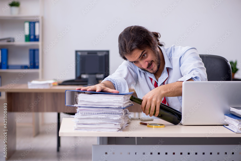 Young male employee drinking alcohol in the office Young male employee drinking alcohol in the office