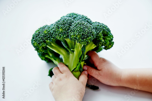 Concept of proper nutrition from childhood Сhild's hands holds a broccoli cabbage. View from above. 