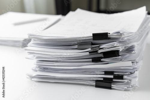 Piles of white papers work large piles of papers stacked together. On the desk in the office with black clip. Documents that are not finished. Business concept.