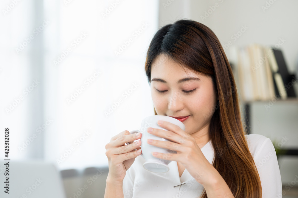 Young asian beautiful business woman working with laptop sitting at home drinking coffee. Smiling charming happy young female doing homework meeting conference with team at home. Young asian beautiful business woman working with laptop sitting at home drinking coffee. Smiling charming happy young female doing homework meeting conference with team at home.