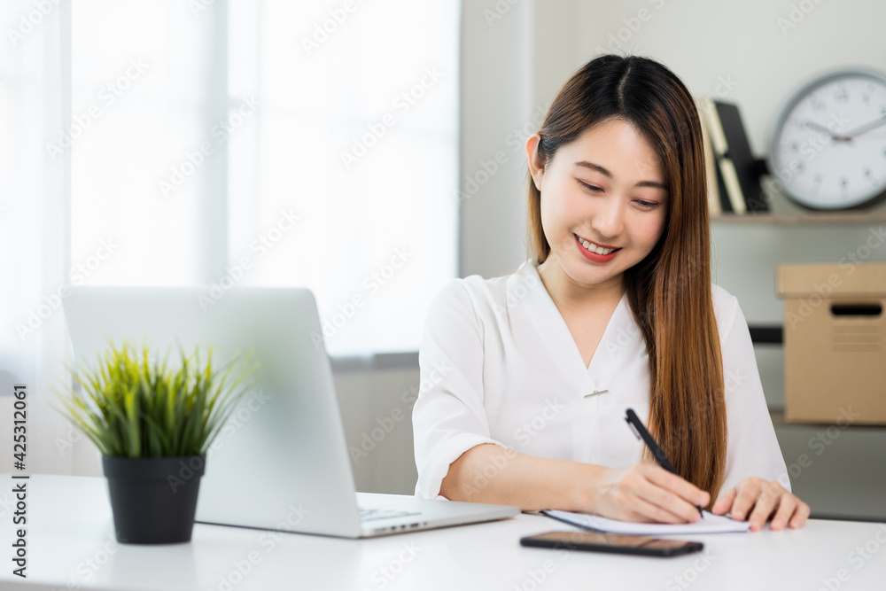 Young asian beautiful business woman working with laptop sitting at home and note on book. Smiling charming happy young female doing homework meeting conference with team at home.