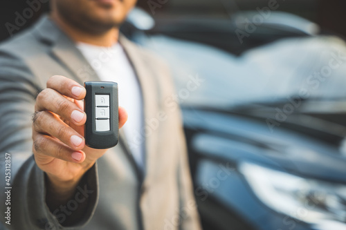 Close up businessman in suit his hands showing or giving car key for customer getting new car. Buy sell rent car concept.