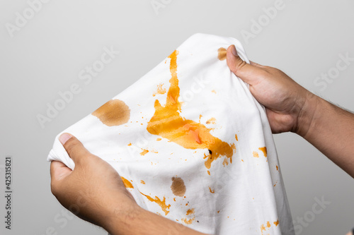 White cotton shirt So many stains and dirt. Stained ketchup The man's hand held the shirt and opened it to look at the dirt.