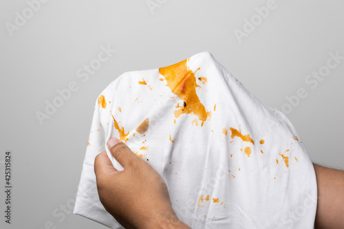White cotton shirt So many stains and dirt. Stained ketchup The man's hand held the shirt and opened it to look at the dirt.