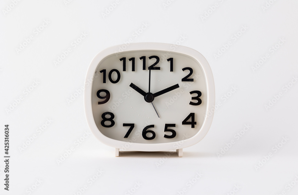 Small white alarm clock, black numbers, set the time for 10.10 o'clock, placed on a white table. Small white alarm clock, black numbers, set the time for 10.10 o'clock, placed on a white table.