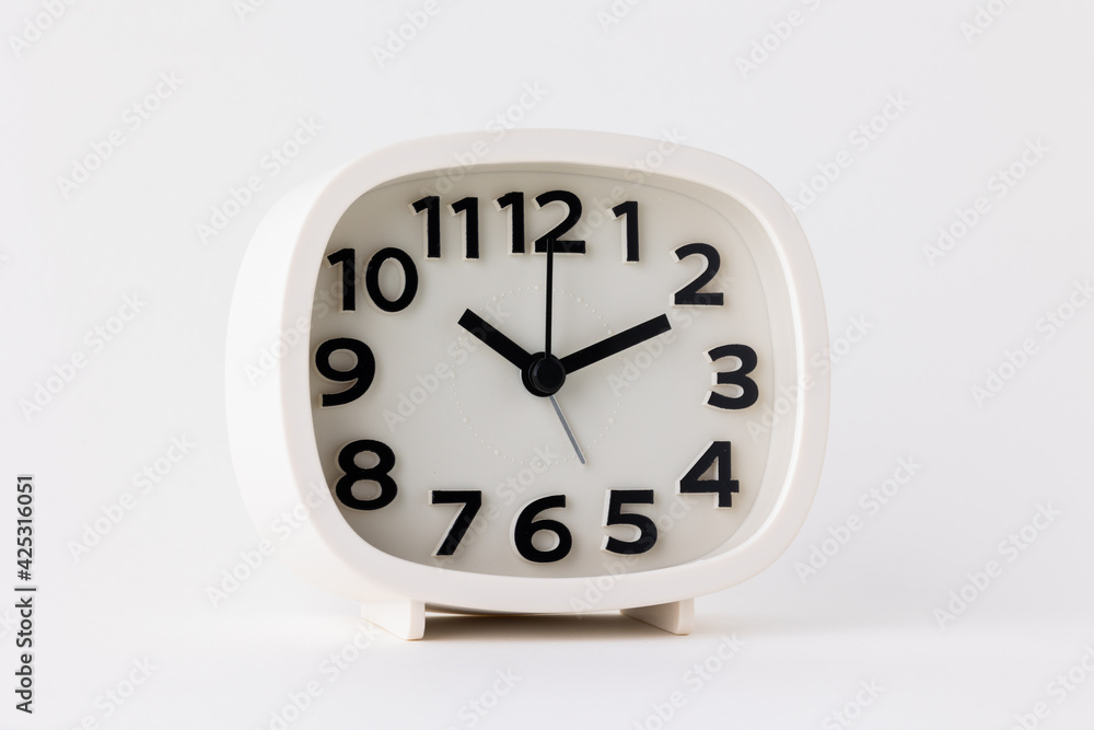 Small white alarm clock, black numbers, set the time for 10.10 o'clock, placed on a white table. Small white alarm clock, black numbers, set the time for 10.10 o'clock, placed on a white table.