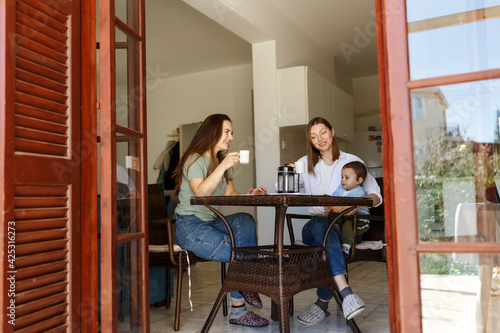 Mother With baby boy son talking to Friend In Kitchen while drinking coffee. Lifestyle, friendship and communication concept