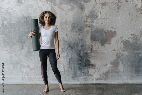 Young afro american woman standing with exercise mat in fitness center