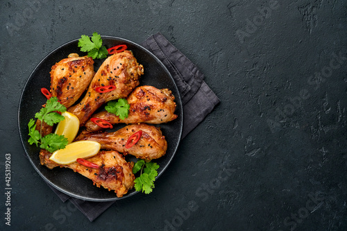 Grilled chicken drumsticks or legs or roasted bbq with spices and tomato salsa sauce on a black plate. Top view with copy space.