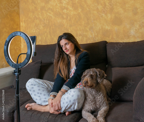 mujer haciendo videoconferencia con su móvil para una Reunión de trabajo en casa, sentada en el sofá teletrabajando con su perro haciendole compañia