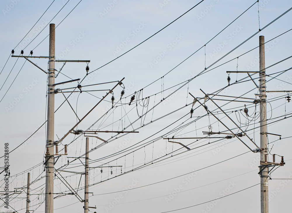 Catenary railway traction. Overhead line, electricity pylons on railway track against blue sky. High voltage transmission. Supplying electricity for trains, with a pylon pillar in the background. Catenary railway traction. Overhead line, electricity pylons on railway track against blue sky. High voltage transmission. Supplying electricity for trains, with a pylon pillar in the background.