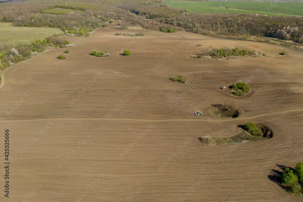 Obraz premium Aerial view large tractor cultivating a dry field. Top down aerial view tractor cultivating ground and seeding a dry field. Aerial tractor cuts furrows in farm field for sowing