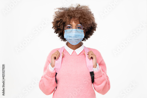 Studio portrait of african american school girl or college student with curly afro hair wearing face mask and glasses, isolated on gray background © Damir Khabirov