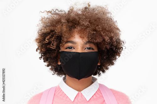 Headshot of smiling african american school girl or college student with curly afro hair wearing black cotton mask, isolated on gray background