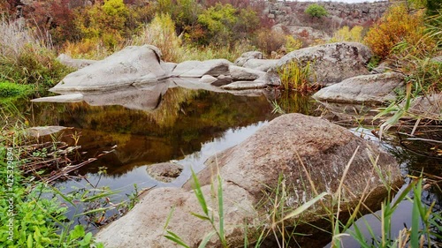 Autumn trees and large stone boulders around. A water cascade in autumn creek with fallen leaves. Water flows around the stones in the river. Aktovsky Canyon, Ukraine. photo