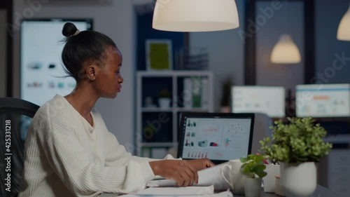 Wallpaper Mural Black manager analysing graphics and financial statistics from documents working overtime in front of laptop sitting in start-up business office. Focused employee respecting deadline of project Torontodigital.ca