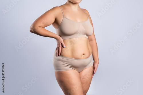 Fat woman in beige underwear on gray background, overweight female body