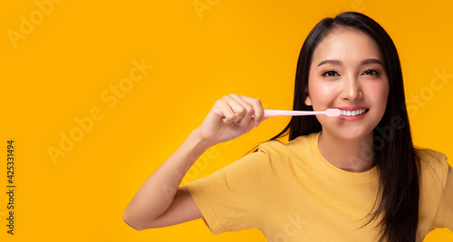 Happy woman brushing beauty tooth using toothbrush Young lady has beauty teeth Beautiful asian girl get strong tooth white teeth and nice tooth alignment Yellow background, copy space Dental care