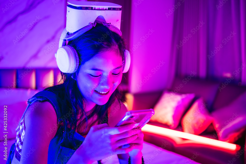 Young asian woman is using virtual reality headset. Neon light studio portrait. Concept of virtual reality, simulation, gaming and future technology.Asian woman play game in bedroom. Young asian woman is using virtual reality headset. Neon light studio portrait. Concept of virtual reality, simulation, gaming and future technology.Asian woman play game in bedroom.