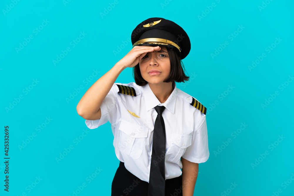 Young airplane pilot over isolated blue background looking far away with hand to look something Young airplane pilot over isolated blue background looking far away with hand to look something