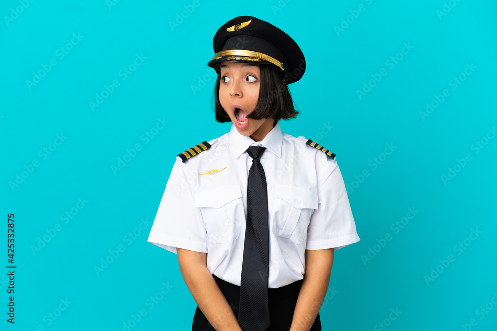 Young airplane pilot over isolated blue background doing surprise gesture while looking to the side Young airplane pilot over isolated blue background doing surprise gesture while looking to the side