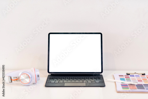 Tablet blank white screen is placed at the work desk with color swatch at the office. Mock up.