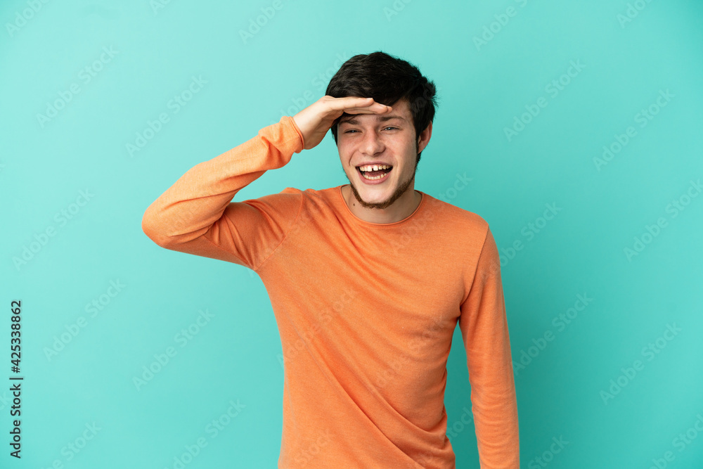 Young Russian man isolated on blue background looking far away with hand to look something Young Russian man isolated on blue background looking far away with hand to look something