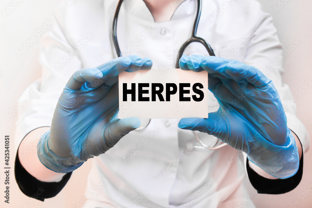 The doctor's blue - gloved hands show the word HERPES - . a gloved hand on a white background. Medical concept. the medicine The doctor's blue - gloved hands show the word HERPES - . a gloved hand on a white background. Medical concept. the medicine