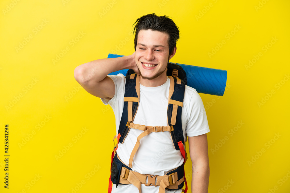 Young mountaineer Russian man with a big backpack isolated on yellow background laughing Young mountaineer Russian man with a big backpack isolated on yellow background laughing