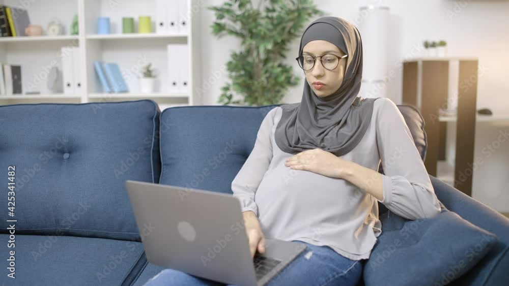 Pregnant muslim employee in hijab working on laptop at home, business career Pregnant muslim employee in hijab working on laptop at home, business career