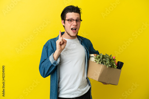 Russian Man making a move while picking up a box full of things isolated on yellow background intending to realizes the solution while lifting a finger up